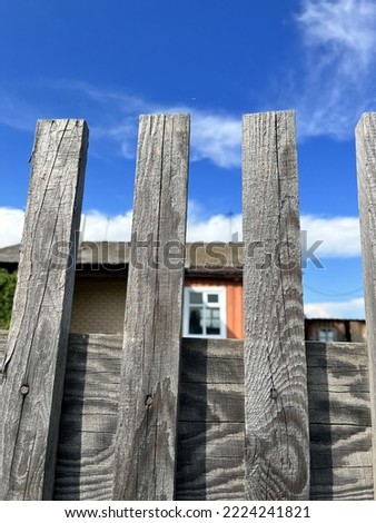 Wooden fence in the village, blackened over time. Against the background of the blue sky.