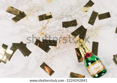Christmas tree baubles in the shape of a green champagne bottle lying on a marble table. Glitter and golden stars decorate the picture.