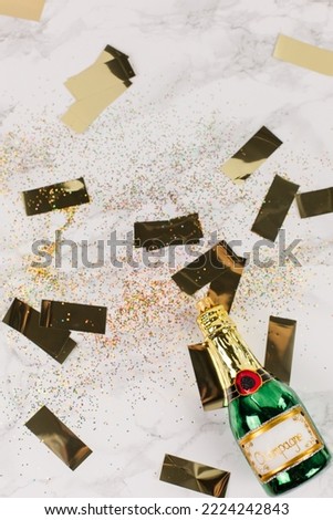 Christmas tree baubles in the shape of a green champagne bottle lying on a marble table. Glitter and golden stars decorate the picture.