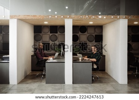 Wide angle view of two freelance business men working in cubicle styled co working office space. Royalty-Free Stock Photo #2224247613
