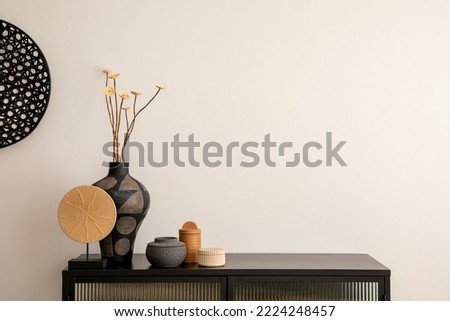 Minimalist composition of living room interior with copy space, black commode, vase with dried flowers, decoration on the wall and stylish personal accessories. Home decor. Template. 
 Royalty-Free Stock Photo #2224248457
