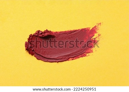 Smear of bright lipstick on yellow background, top view