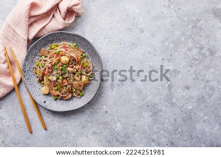 Wok with turkey meat, soba noodles, corn, green peas, green beans and carrots served on gray background with chopsticks. Asian food, concept of street food. Top view with copy space Royalty-Free Stock Photo #2224251981