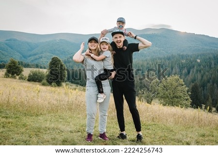 Mother, father hug childs in autumn. Family with kids hiking on grass on top of a mountains. Tourists enjoy valley view sunset. Mom, dad, son, and daughter. Holiday trip concept. World Tourism Day.