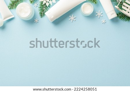 Winter season skin care concept. Top view photo of white cosmetic bottles pine branches christmas ornaments and snowflakes on isolated pastel blue background with blank space
