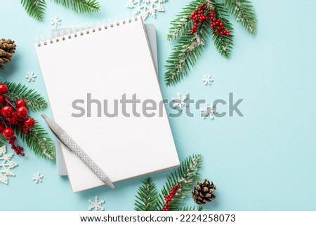 Christmas Eve concept. Top view photo of notepad pen spruce branches in hoarfrost pine cones mistletoe berries and snowflakes on isolated pastel blue background with empty space