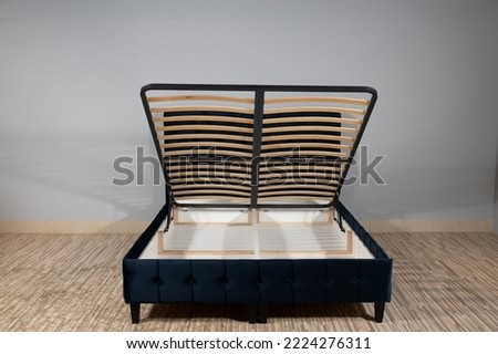 A dark blue bed with a storage space revealed by lifting the wooden slatted base