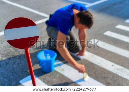 Road service worker paints striped pedestrian crossing on asphalt with paint brush. Markings for pedestrians on roadway. Safe transition for people. Real workflow..