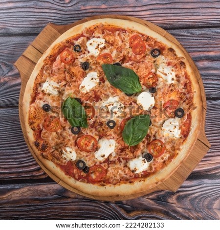 Pizza with tomato sauce, tomatoes, olives, mozzarella, cheddar cheese and basil leaves on a wooden table