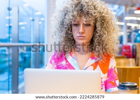 Portrait of a young Caucasian woman with curly blonde hair, working in a coffee shop with her laptop and smart phone