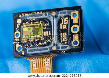 Optoelectronic image sensor of optical laser computer mouse on a blue background. Modern green silicon die with photodiodes array and gold wires on dark PCB with orange flexible printed circuit cable. Royalty-Free Stock Photo #2224293013
