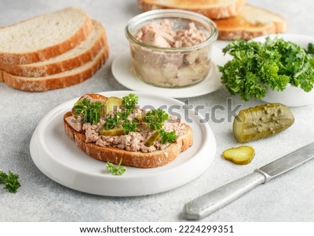 Cod liver in a jar and sandwich with liver, pickled cucumber and parsley on a white plate on a gray concrete background. Breakfast, brunch. Natural source of omega 3 and vitamin D. Selective focus