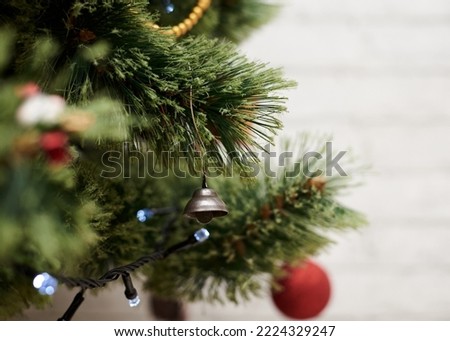Close up picture of christmas ornaments on green artificial Xmas tree. Red baubles balls, jingle bell, bead garland and christmas lights hanging on pine. Holiday atmosphere. New year celebration.