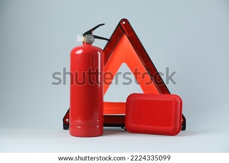 Emergency warning triangle, red fire extinguisher and first aid kit on light grey background. Car safety Royalty-Free Stock Photo #2224335099