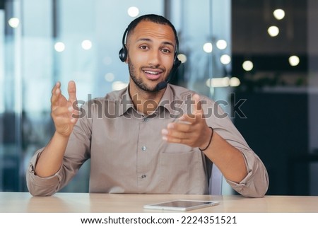 Webcam view, happy african american man talking online video call looking at camera using headset, man working inside modern office building tech support and helpline call center. Royalty-Free Stock Photo #2224351521