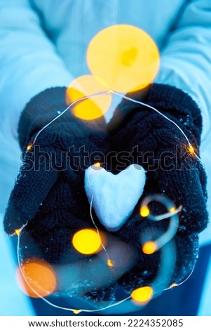 An abstract photo of love. A pair of lovers holding each other's hands and a heart-shaped snowball in their hands.