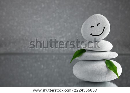 Stack of stones with drawn happy face and leaves on grey background, space for text. Zen concept