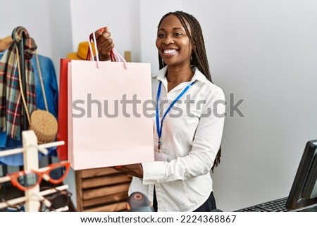Young african american shopkeeper woman smiling happy holding shopping bags at clothing store.