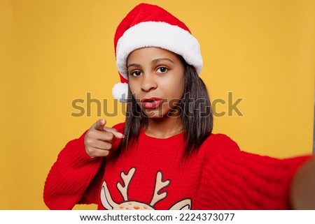 Close up merry little kid teen girl 13-14 year old wears red xmas sweater Santa hat posing do selfie shot pov mobile cell phone isolated on plain yellow background. Happy New Year 2023 holiday concept