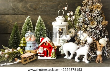 Festive card, christmas and new year atmosphere, decorative home decoration.  On a wooden background are green Christmas trees, golden cones, figurines of white deer, Santa's house and a snowman.