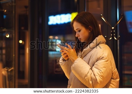 Young hipster girl indoor in trendy wear using smartphone scrolls social media feed, chats with friends in instant messengers. Side view Royalty-Free Stock Photo #2224382335