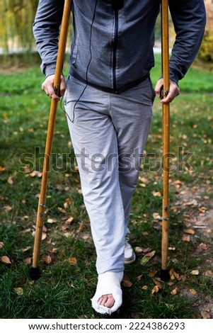 A young man with a broken leg, walking on crutches.