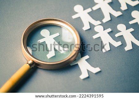 Magnifying glass placed on the table with group of paper human dolls, and only one in the focus, man replacement and management, leadership person, HR concept Royalty-Free Stock Photo #2224391595