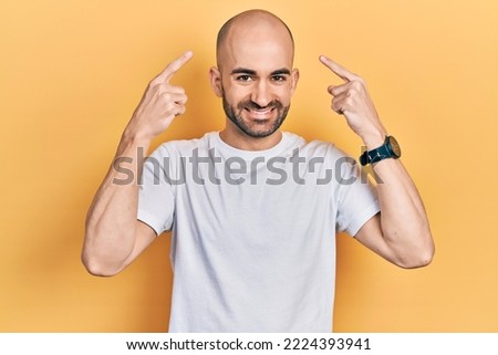 Young bald man wearing casual white t shirt smiling pointing to head with both hands finger, great idea or thought, good memory  Royalty-Free Stock Photo #2224393941