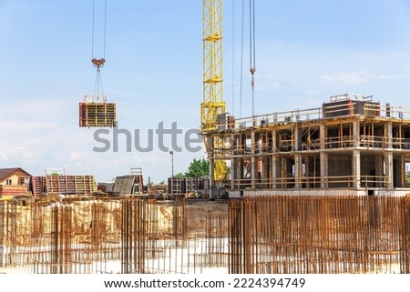 Crane and building construction site against blue sky. Concrete building under construction. In the foreground is the steel reinforcement of the foundation of the future building.
