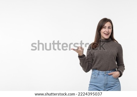 A young positive woman points with her thumb at copy space a white background.An excited, shocked woman shows a place to copy and place an advertisement or advertising text, banner