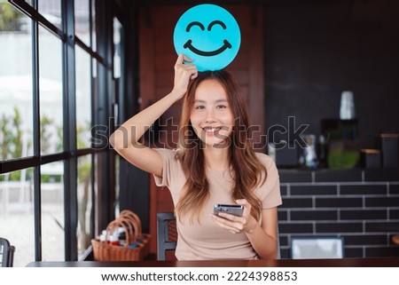 Asian woman holding blue happy smile face on paper cut, user giving good feedback rating, think positive , customer review, assessment, of mental health day, Compliment Day, satisfaction concept. Royalty-Free Stock Photo #2224398853