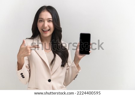 Portrait photo of young beautiful Asian woman feeling happy or surprise shock pointing at smart phone with black empty screen on white background can use for advertising or product presenting concept.