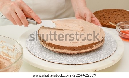 Assembling the cake. Woman hands topping part of the cake with chocolate cream. Step by step chocolate cake recipe, close up baking process