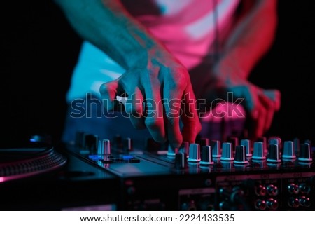 Disc jockey mixing techno music on rave party. Club dj playing set on stage. Disk jokey adjusting volume frequency regulator on sound mixer  Royalty-Free Stock Photo #2224433535