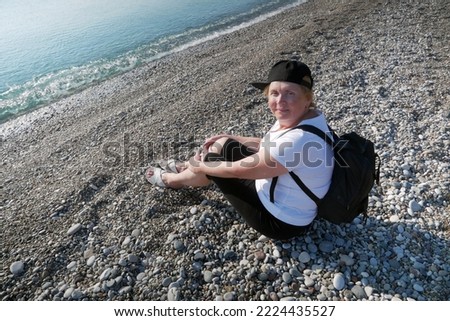 Senior adventureisageless woman with backpack on the sea beach. Summer active tourism for pensioner. Outdoors
