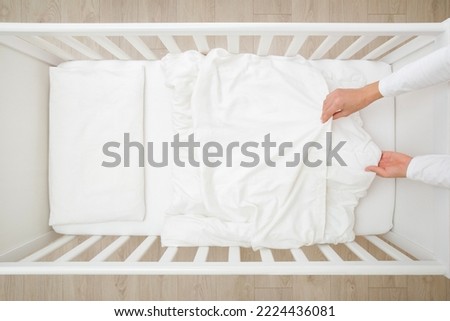 Young adult mother hands changing white blanket cover in baby crib. Regular bed linen change. Closeup. Top view.  Royalty-Free Stock Photo #2224436081