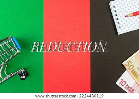REDUCTION - word (text) and euro money on a table of different colors, a trolley, a basket of grocery notepad and a red pencil. Business concept, buying, selling, supermarket, store (copy space).