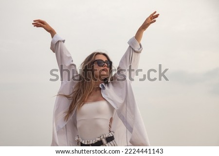 Portrait happy young woman in casual white shirt and sunglasses arms raised at summer beach. Relaxing, fun and enjoy holiday at tropical sea. Concept of beach holidays, summer vacation. Copy space