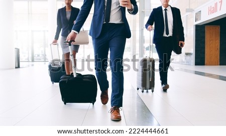 Our business requires us to travel. Cropped shot of three unrecognizable businesspeople walking and pulling suitcases while in the office during the day. Royalty-Free Stock Photo #2224444661