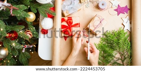A girl decorates a Christmas present, Hands close-up holding scissors. Decorate gifts for the holiday on the table next to the decorated Christmas tree, Christmas, New Year,