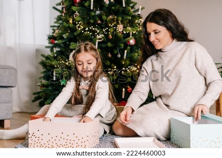 Excited daughter and mother sitting at home near beautiful decorated Christmas tree and enjoying opening their presents. Family holidays. Festive christmas mood. Selective focus.