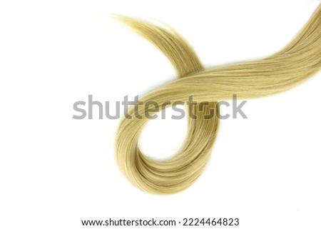 Blond shiny hair wave, on white. Blonde hair lock tied in knot. Strand of honey blonde hair on white background, top view Royalty-Free Stock Photo #2224464823