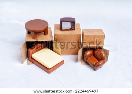 Tiny delivery boxes and miniature furniture figurines isolated on gray background. Moving and furniture shipping concept. Royalty-Free Stock Photo #2224469497