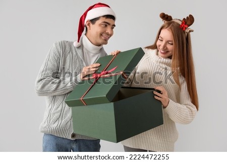 Happy young couple opening Christmas present on grey background