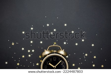 Golden vintage alarm clock decorated with star confetti on dark background. Bedtime stories concept. Selective focus, copy space.