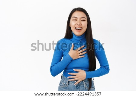Portrait of laughing asian girl smile, chuckle, looking at smth funny, standing over white background.