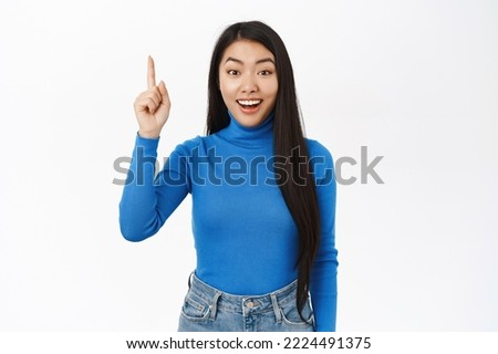 Portrait of stylish korean girl points up, smiles and looks excited, shows banner, advertisement, stands over white background.