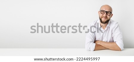 Smiling young man in glasses sitting at the table on a white background. Banner.