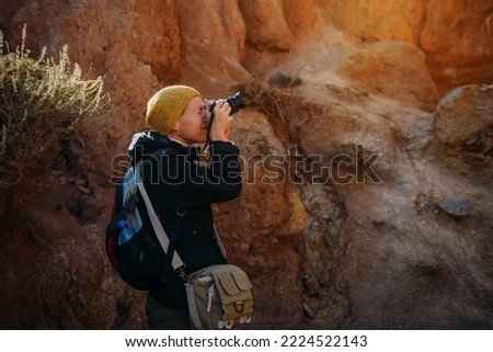 Nature photographer taking pictures of canyon at sunset. Traveling woman takes photos in mountains. Happy female tourist with digital camera.