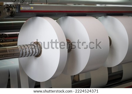 The process of winding paper self-adhesive tape into rollers of printing offer paper for printing houses. Close-up of the paper cutting and rewinding machine. Selective focus Royalty-Free Stock Photo #2224524371